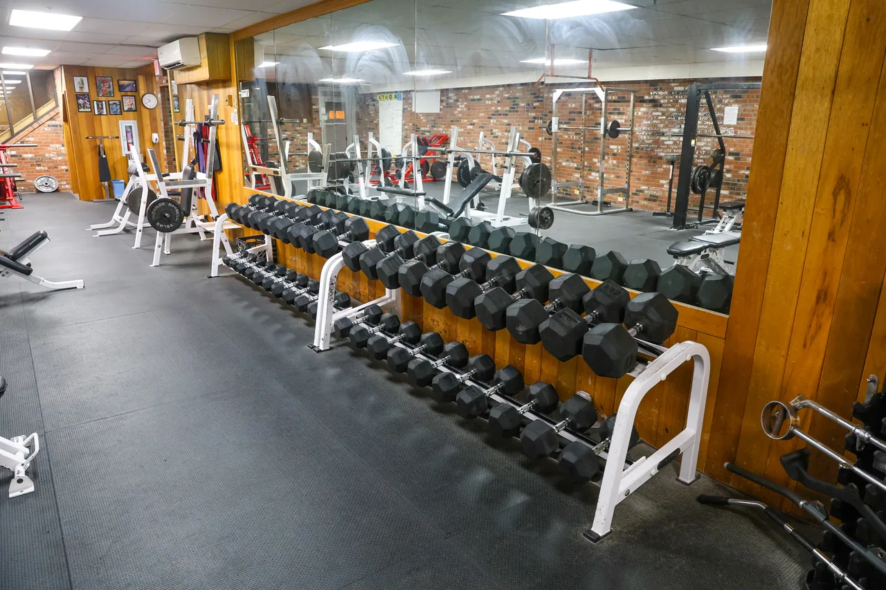 A full dumbbell rack in RecFit's weight room, squat racks and benches in the mirror