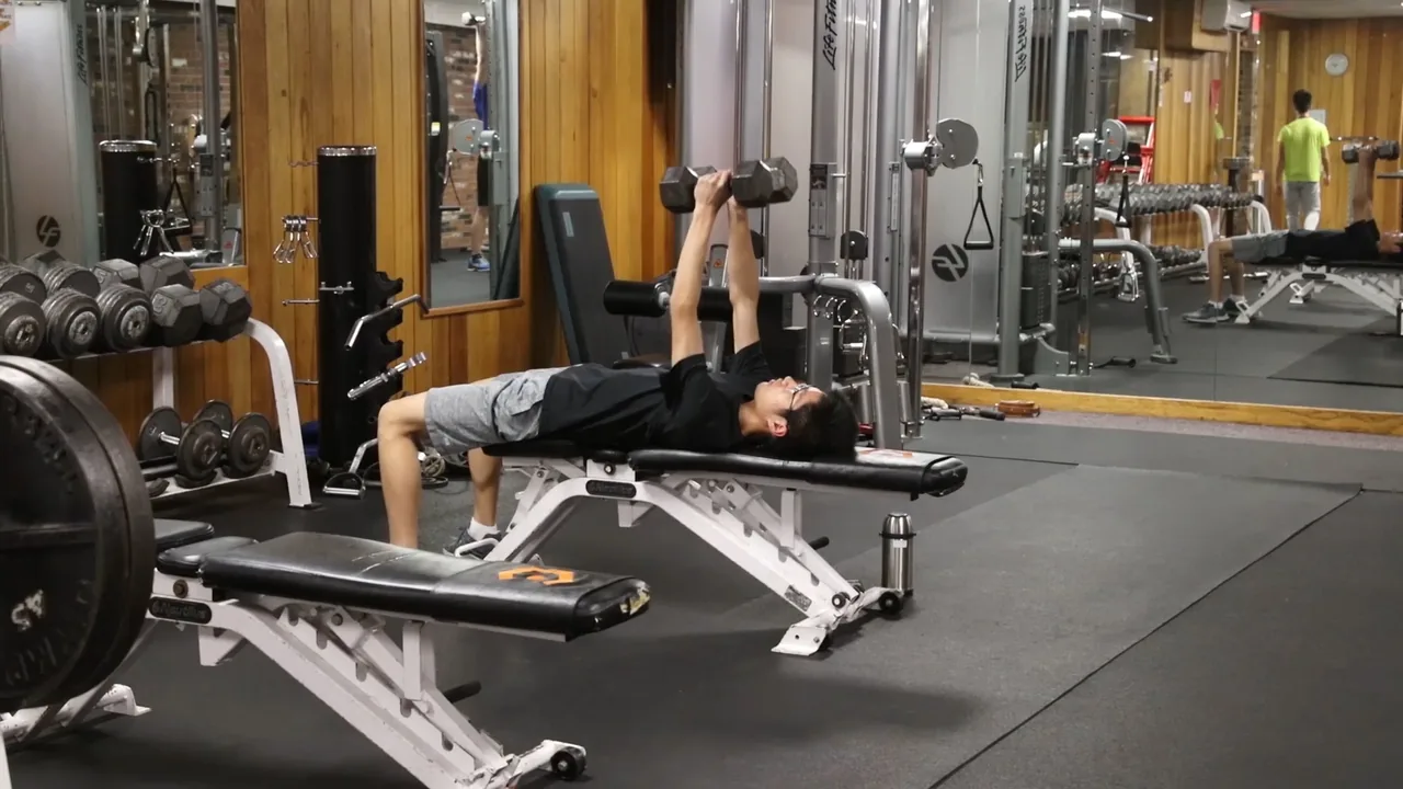 A member pressing dumbbells on a bench in RecFit's weight room